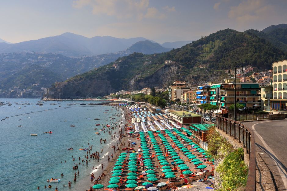 A lively summer day at Sorrento's coastline with colorful umbrellas and mountains.