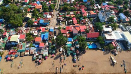A vibrant aerial view of a coastal town in the Philippines, showcasing colorful rooftops, beachfront, and local boats.