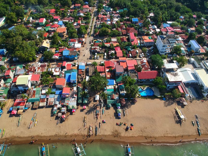 A vibrant aerial view of a coastal town in the Philippines, showcasing colorful rooftops, beachfront, and local boats.