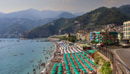 A lively summer day at Sorrento's coastline with colorful umbrellas and mountains.