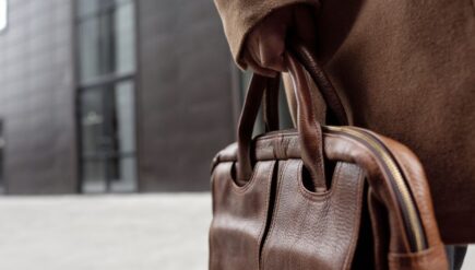 Close-up of a stylish leather briefcase being held by a person in winter attire.