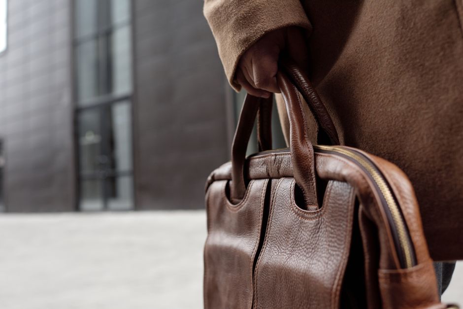 Close-up of a stylish leather briefcase being held by a person in winter attire.